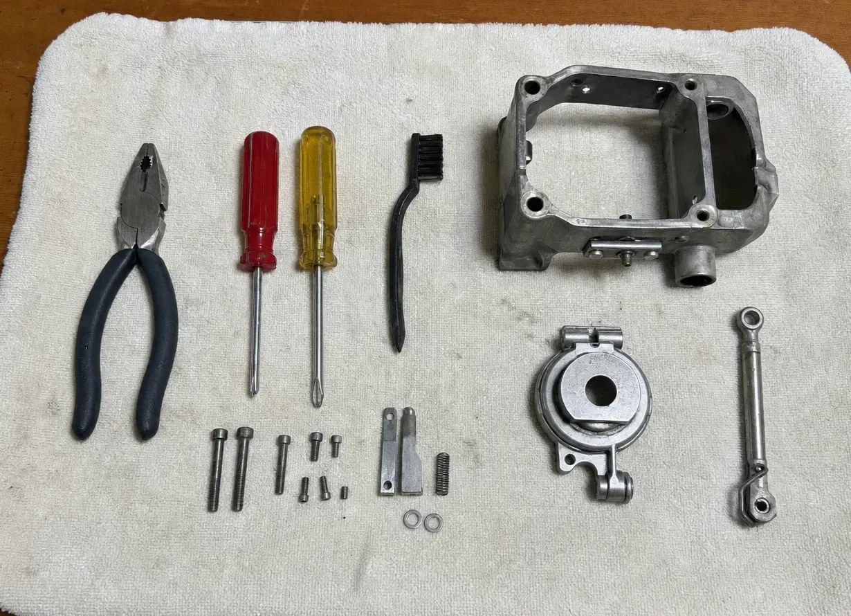 Pliers, two coloured-handle screwdrivers and a brush laid beside a cast housing, a round ring-shaped part, bolts and a spring